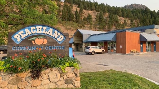 Exterior of Peachland Community Centre. There is signage for the community centre and there are mountains in the background.