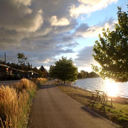 Paved walkway near water. The sun is setting in the background.