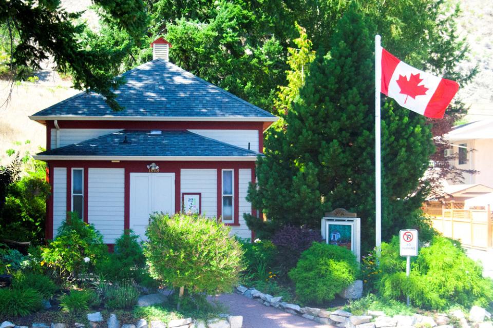 Exterior of Peachland's Little Schoolhouse. There is a small wooden building with a Canadian flag on a pole.